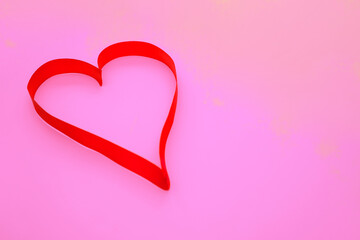 On a pink background, a pink satin ribbon in the shape of a heart.Gift wrap.