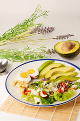 The big salad consists of sliced avocado, boiled egg, lettuce, lettuce, tomato and biscuits, topped with salad cream, avocado cut in half on the back, A meal with a lot of vegetables.