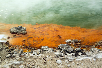 Obraz na płótnie Canvas Orange rock in hot water from which steam rises, deposits of minerals along the shore of the spring