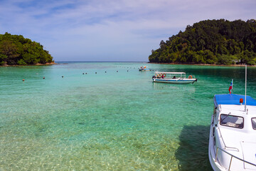 Transparent turquoise sea water in the foreground, boat on the water, tropical vegetation jungle in...
