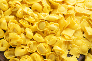 Tartollini with cheese or meat for cooking in broth, different shapes. Traditional dish for celebrations in italy, Emilia Romagna region. Fresh homemade pasta with filling on a wooden table.