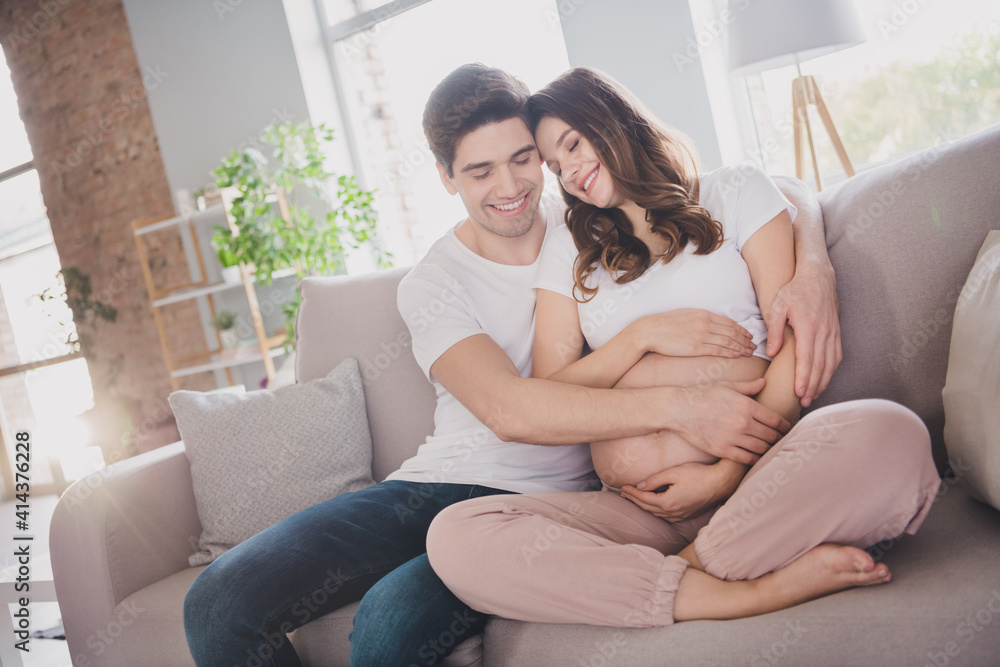 Sticker Photo of dreamy adorable cute good mood couple expecting child sitting couch embracing belly inside indoors