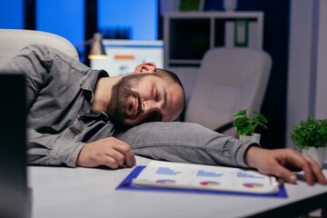 Obraz premium Hardworking entrepreneur sleeps on table at workplace because of deadline. Workaholic employee falling asleep because of while working late at night alone in the office for important company project.