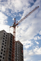 A crane near a house under construction against the blue sky.