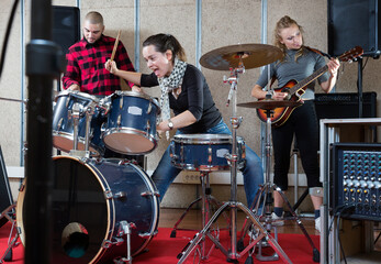 Music garage band with expressive young girl drummer rehearsing in sound studio