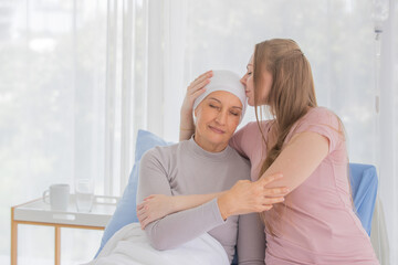 Woman and female cancer patient cuddle and kiss together for the symbol of support and...