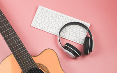 computer keyboard, headphones and acoustic guitar on pink background with copy space. Musician, leisure  and online music learning  concept.