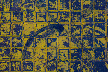 The texture of a manhole cover drenched in yellow paint.