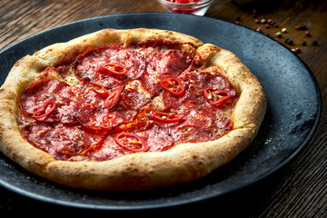 Wood-fired pizza with spicy chorizo salami and chili with crispy sides, served on a black plate on a wooden background. pizzette a kind of Italian pizza