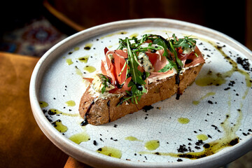 Bruschetta with prosciutto, gorgonzola and arugula on rye bread, served in a white plate. Restaurant food. View from above. Italian cuisine