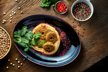A classic oriental appetizer dish - chickpea hummus with falafel, served on a black plate on a wooden background. Restaurant food