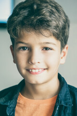 Portrait of Caucasian little boy with stylish haircut. Cute happy child posing in classroom after lesson, smiling and looking at camera. Front view. People, study and appearance concept