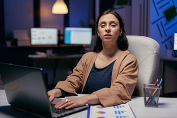 Fototapeta na wymiar Businesswoman holding hands on laptop keyboard looking at camera. Smart woman sitting at her workplace in the course of late night hours doing her job.