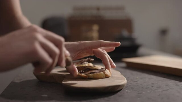man spreading chocolate spread on baguette slices on olive board