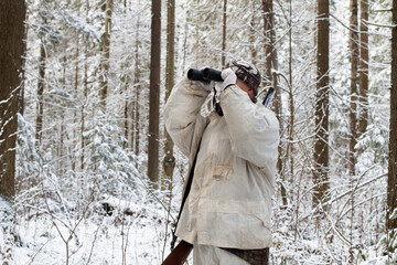 Fototapeta na wymiar hunter in white winter camouflage with binoculars in the forest