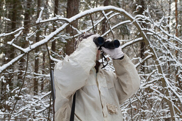 hunter in winter camouflage looks through binoculars