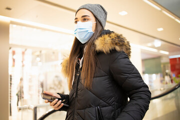 Fototapeta premium Young woman with a protective mask taking the stairs in a shopping mall