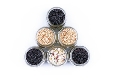 Grains of black rice, buckwheat and other cereals in glass jars, top view on a white background