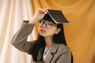 Beautiful asian thai long dark hair woman wearing eyeglasses with a book over head.