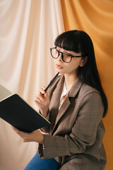 Obraz premium Thoughtful Beautiful asian thai long dark hair woman in jacket suit hold a book and pen.