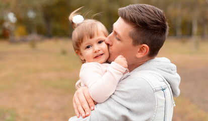 Naklejka na ściany i meble Cheerful young father kissing his little cute daughter outdoor.