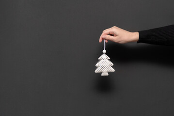 Small Christmas tree toy in the hand on a dark background.