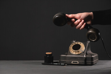 A rotary phone handset in the female hand above the table on the dark background.