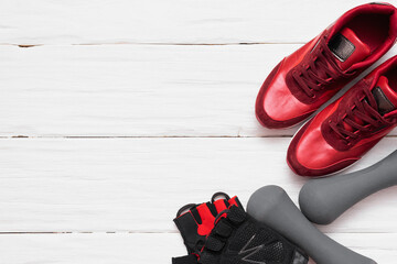 Red sneakers, dumbbells and sport gloves on the white wooden floor background.