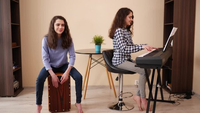Duet music band twin sisters teenager girls play piano and cajon composition at home enjoy spend time together