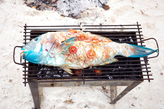 Barbecue, coral fish on the grill. Fresh, raw fish on charcoal stove. Grilling on the beach, freshly caught tropical fish with fresh vegetables. Zanzibar local food.