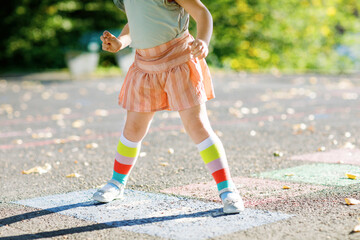 Fototapeta na wymiar Closeup of leggs of little toddler girl playing hopscotch game drawn with colorful chalks on asphalt. Little active child jumping on playground outdoors on a sunny day. Summer activities for children.