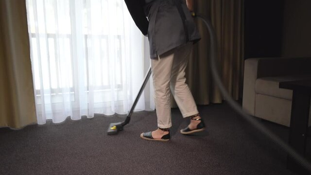 Hotel housekeeper vacuuming carpet covering in hotel suite