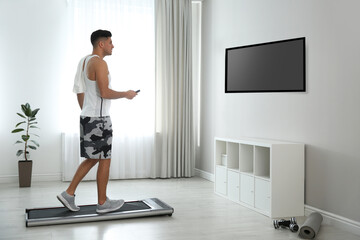 Sporty man training on walking treadmill while watching TV at home