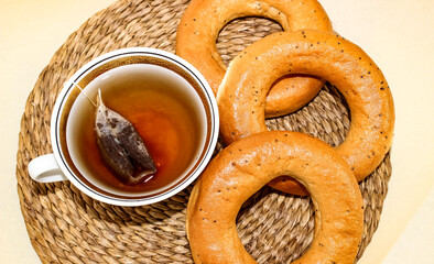A mug of tea is on the table and next to it are ruddy bagels with poppy seeds. Tea party.