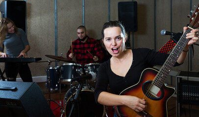 Fototapeta na wymiar Group of young musicians with passionate emotional woman vocalist and guitarist practicing in rehearsal room