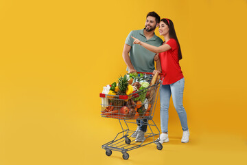 Young couple with shopping cart full of groceries on yellow background © New Africa
