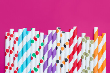 Striped and dotted paper drinking straws on pink background top view