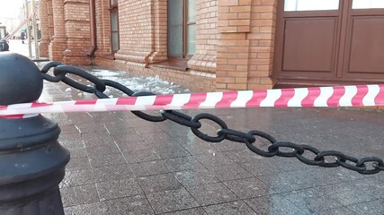 Red and white warning tape in the city near a building from the roof of which ice and icicles are falling. Risk of injury, weather