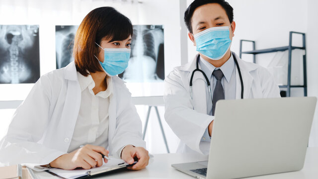 Medical team of asia serious male and young female doctor with protective face masks discussing computed tomography result in hospital office. Social distance, Lifestyle new normal after corona virus.