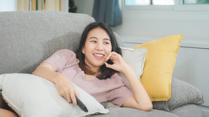 Young Asian teenager woman watching TV at home, female feeling happy lying on sofa in living room....