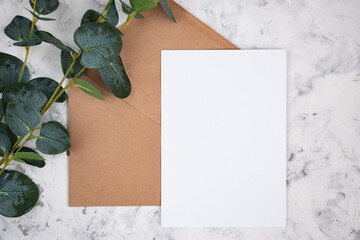 Blank white card, envelope and eucalyptus branch on white marble background. Blank invitation. Flat...