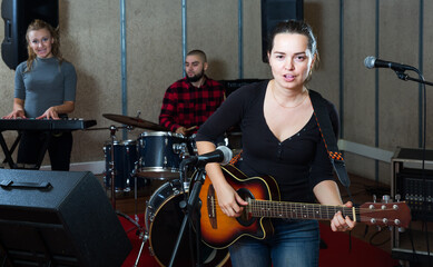 Music garage band with passionate emotional female vocalist and guitarist rehearsing in sound studio
