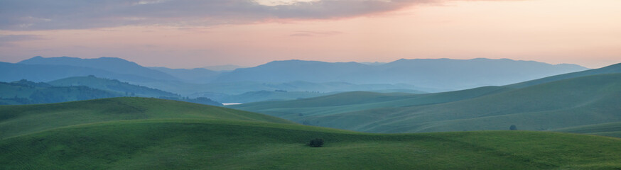 Fototapeta na wymiar Greenery of spring meadows and sunset sky, panoramic view