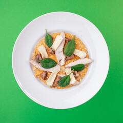 Red lentils with chicken, mushrooms, camembert cheese on white plate on green background. Top view. Close up. Photo for clipping, for the menu