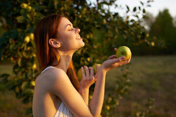 happy woman with green apples in her hands in nature near a tree In the meadow