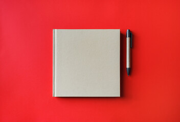 Blank book and pen on red paper background. Blank branding template. Mockup for branding identity for placing your design. Flat lay.