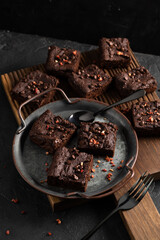 Dark chocolate brownies with choco drops on metal tray on oak cutboard and dark background
