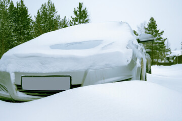 A silver coloured passenger car stands in the snow after a heavy snowfall. A car covered in snow. Snow-covered road. Lots of snow.