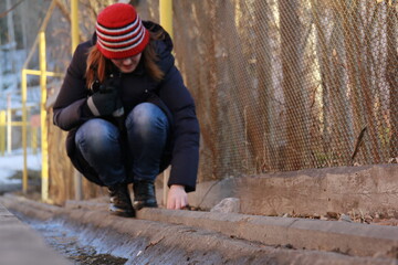 The girl blows leaves along the gutter. Girl over a concrete drainage ditch by the road