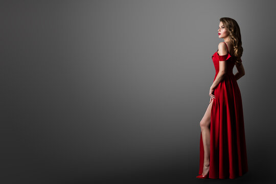 Fashion Woman in Long Red Dress. Model Showing Leg in Evening Silk Slit Gown. Side Profile View. Black Background with Copy Space